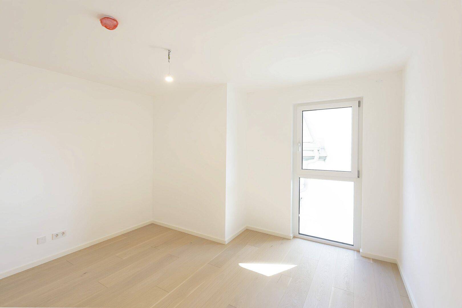 Helles Zimmer mit Holzboden und großem Fenster, ideal als Schlaf- oder Arbeitszimmer.