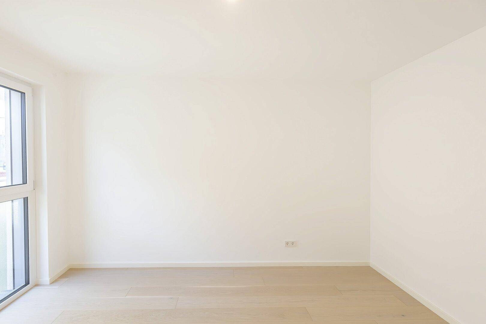 Geräumiges, helles Zimmer mit Holzboden und großem Fenster, vielseitig nutzbar.