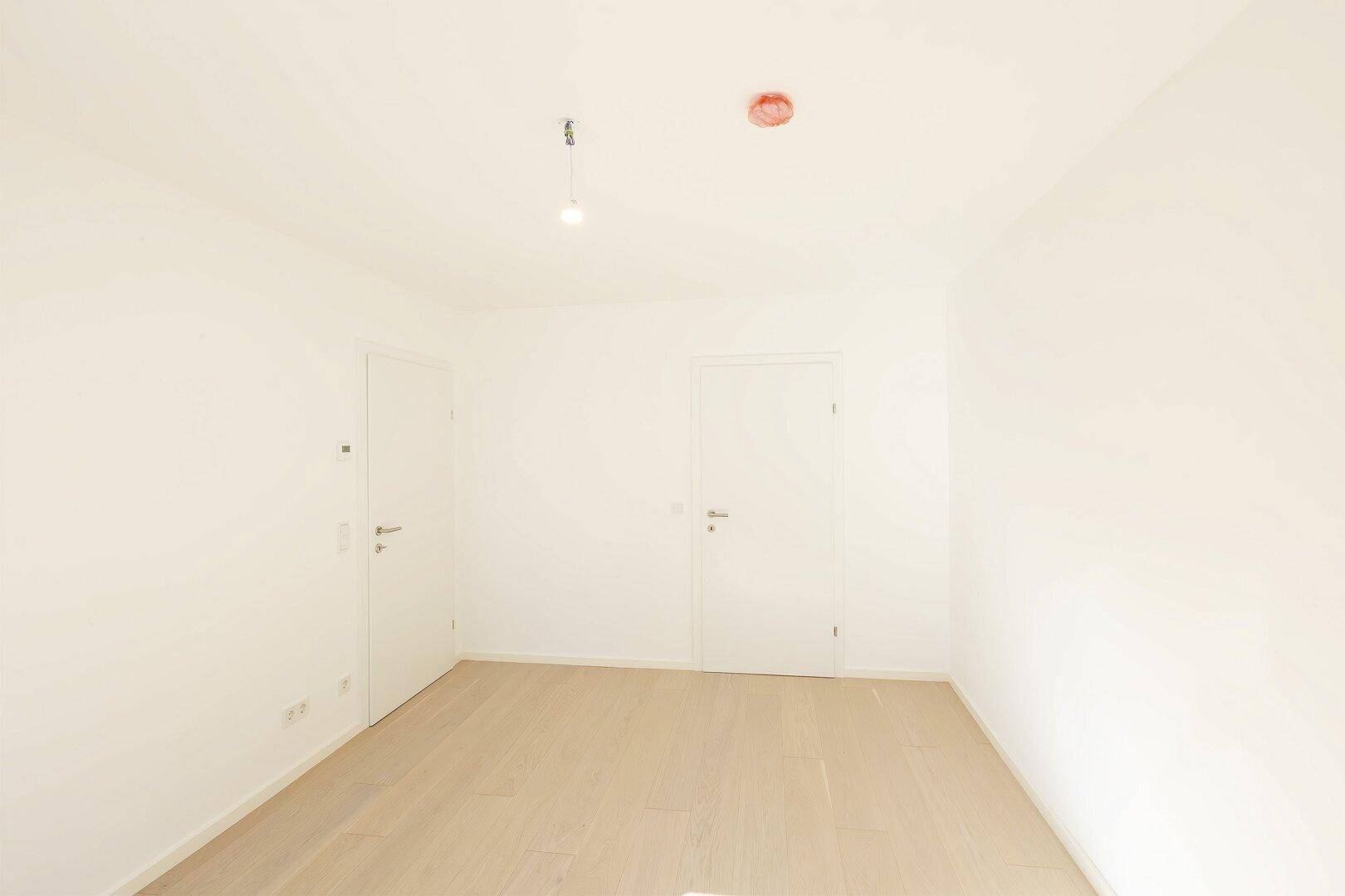 Helles Zimmer mit Holzboden und zwei Türen, bietet flexible Gestaltungsmöglichkeiten.