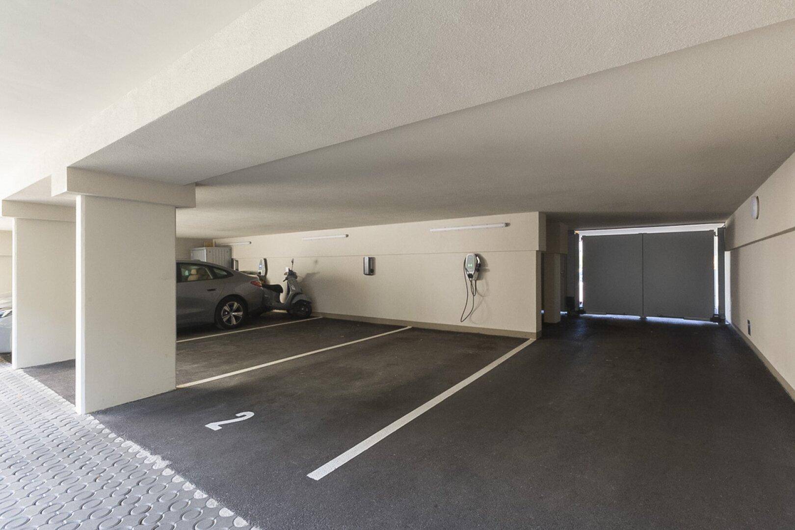 Tiefgarage mit markierten Stellplätzen, einem Auto, einem Roller und Ladestationen für Elektrofahrzeuge.