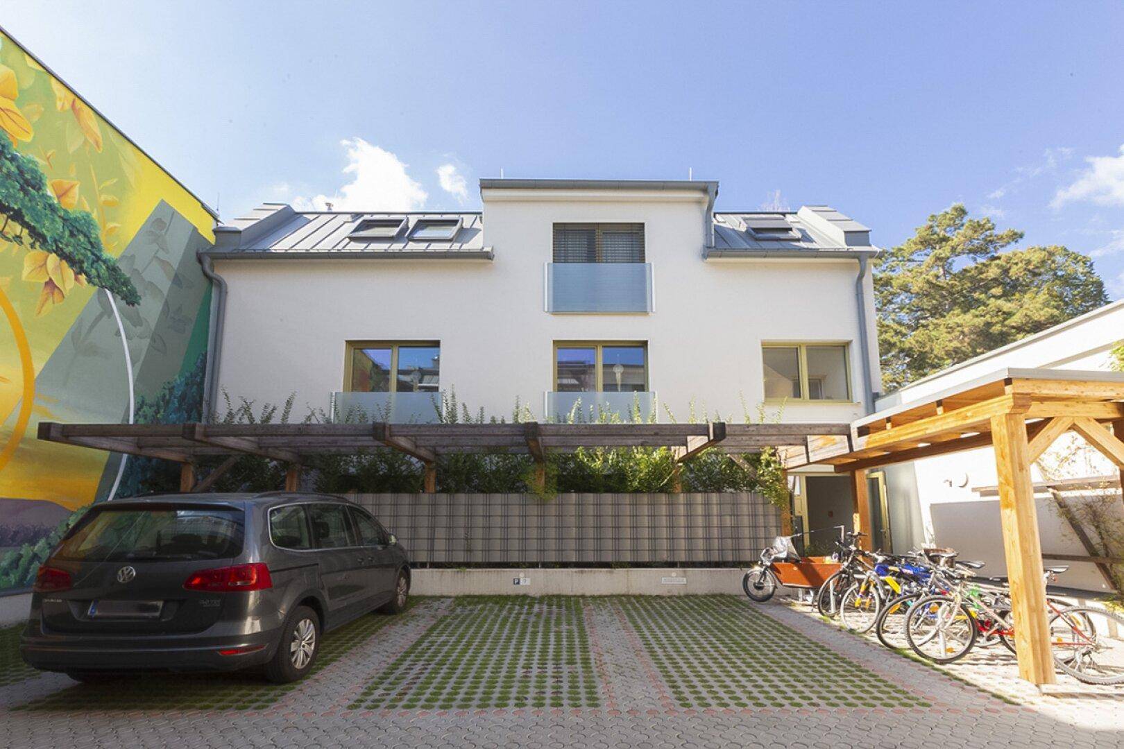 Modernes Gebäude mit Parkplätzen, Carports und Fahrrädern, daneben eine große farbenfrohe Wandmalerei.