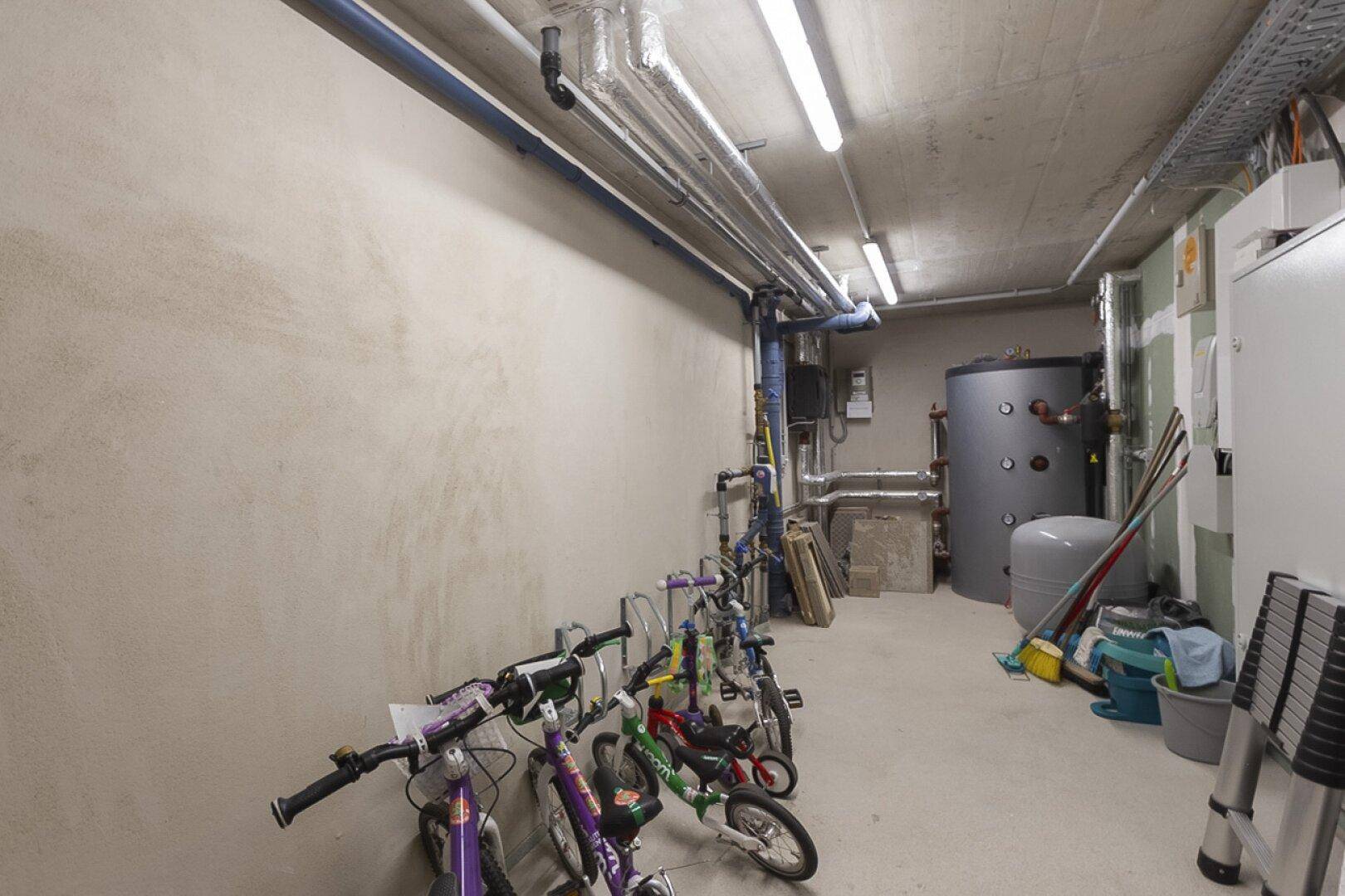 Kellerraum mit sichtbaren Rohren, Warmwasserspeicher und abgestellten Kinderfahrrädern, der als Technik- und Abstellraum dient.