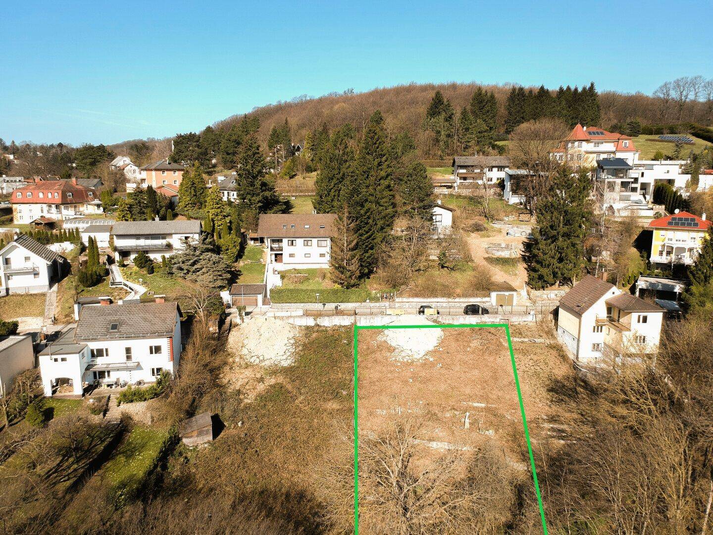 Luftaufnahme eines Grundstücks mit grüner Umrandung an einem Hang, umgeben von Wohnhäusern.
