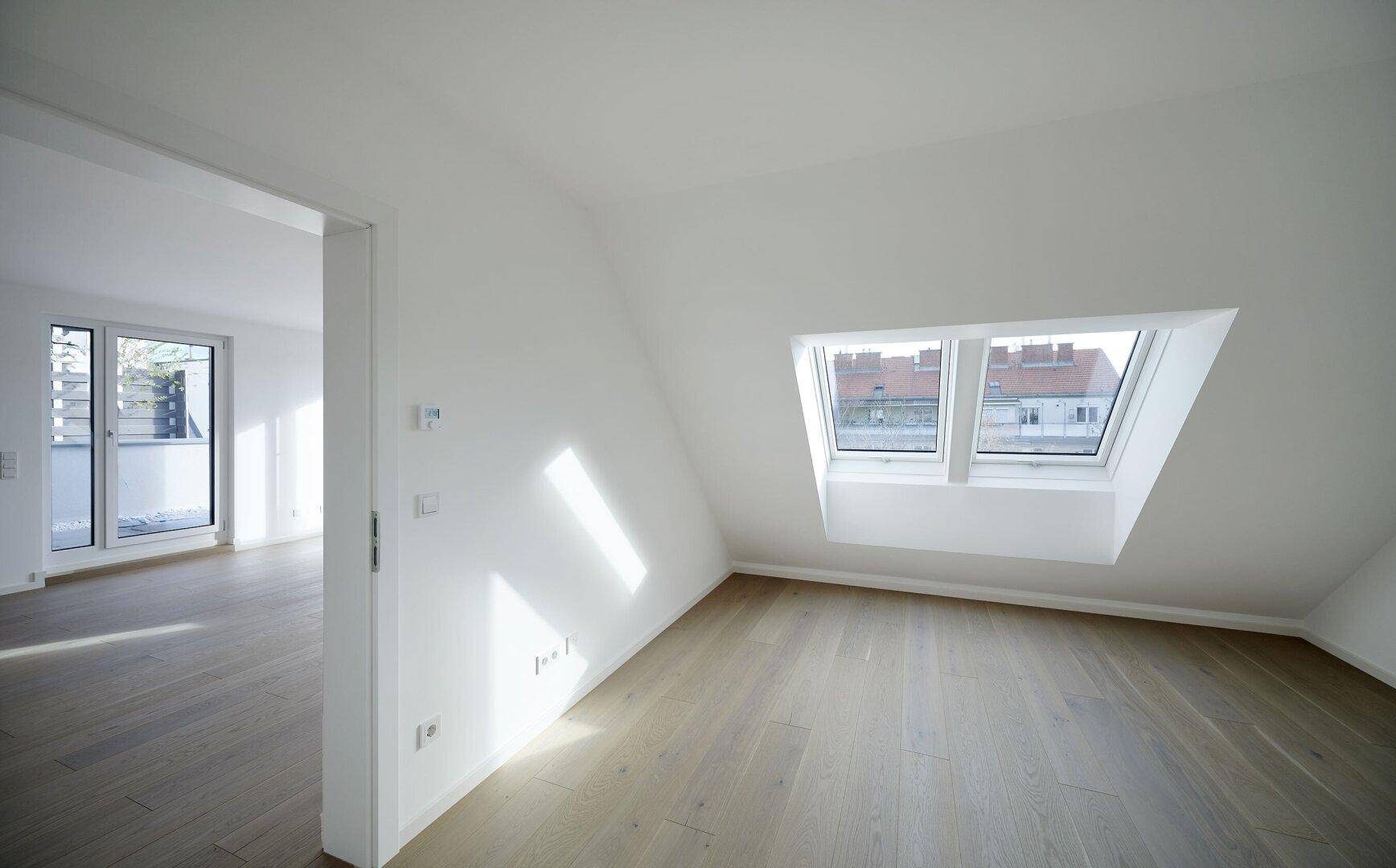 Heller Raum mit Holzboden, Dachschräge und zwei großen Dachfenstern, die viel Licht spenden.