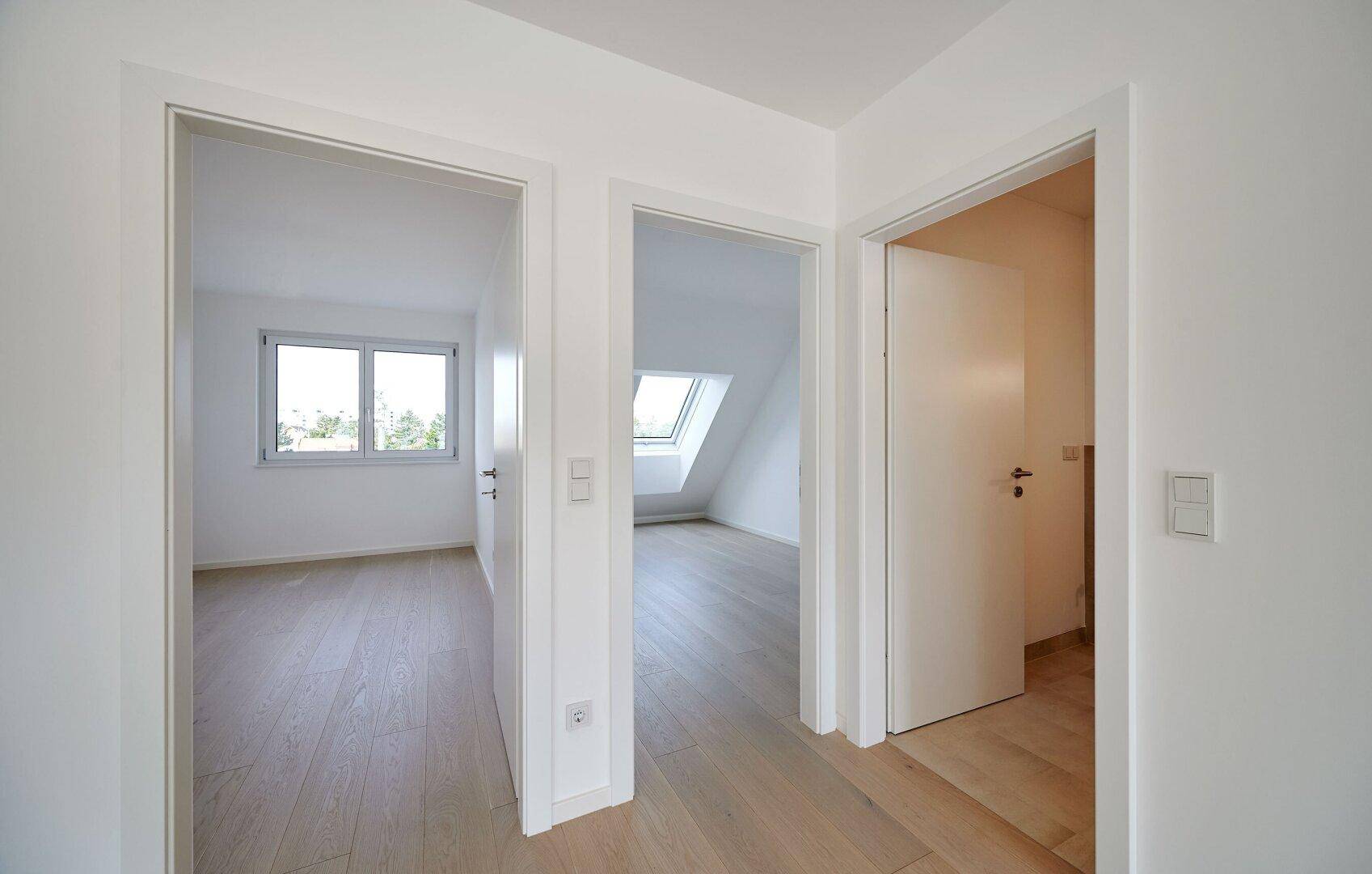 Moderner Flur mit Holzboden und Blick in angrenzende, lichtdurchflutete Räume.