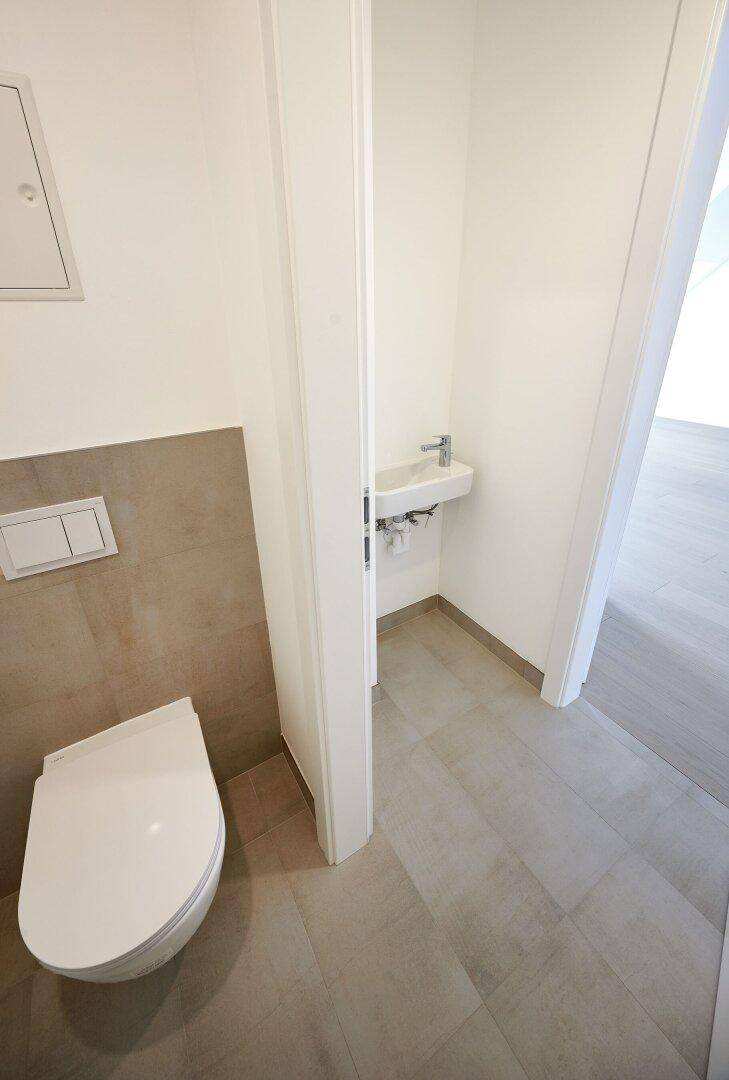 Kompaktes Gäste-WC mit Wand-WC, kleinem Waschbecken und modernen Fliesen.