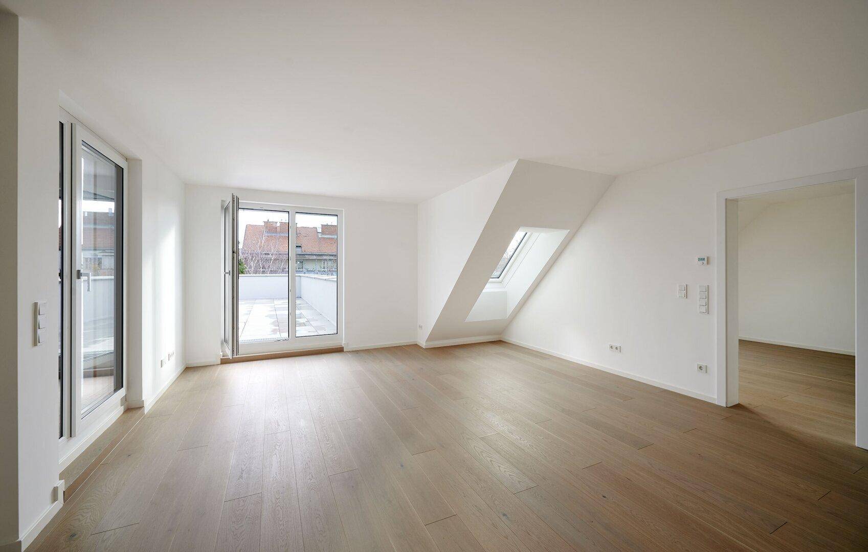 Großzügiger, heller Raum mit Holzboden, Dachschräge und Zugang zur Dachterrasse.