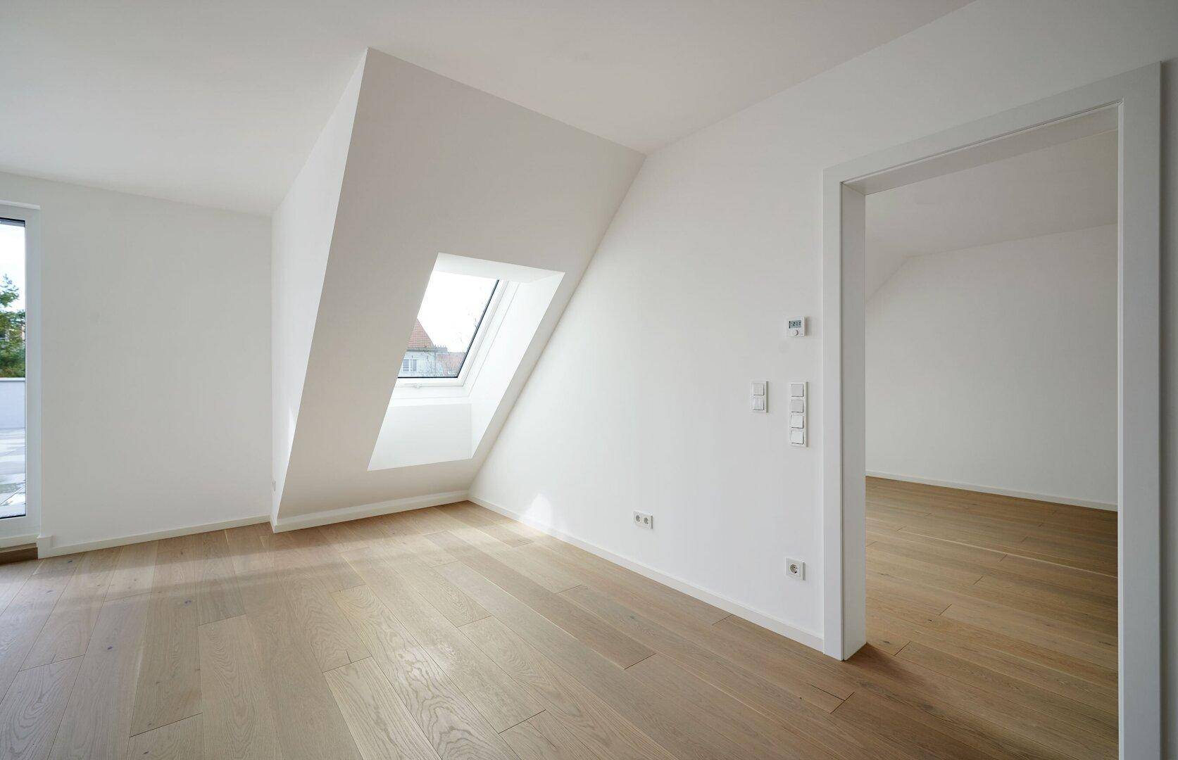 Geräumiges Zimmer mit Holzboden, Dachschräge und Zugang zu einem weiteren Raum.