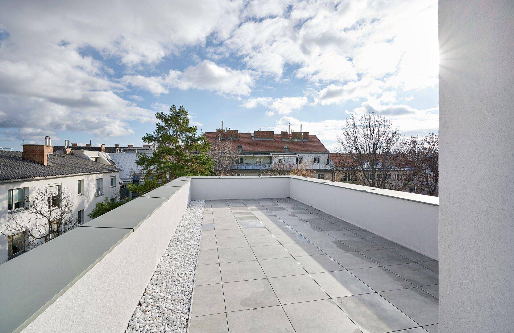 Geräumige Dachterrasse mit hellen Fliesen und Kiesstreifen, bietet einen weiten Blick über die Umgebung.