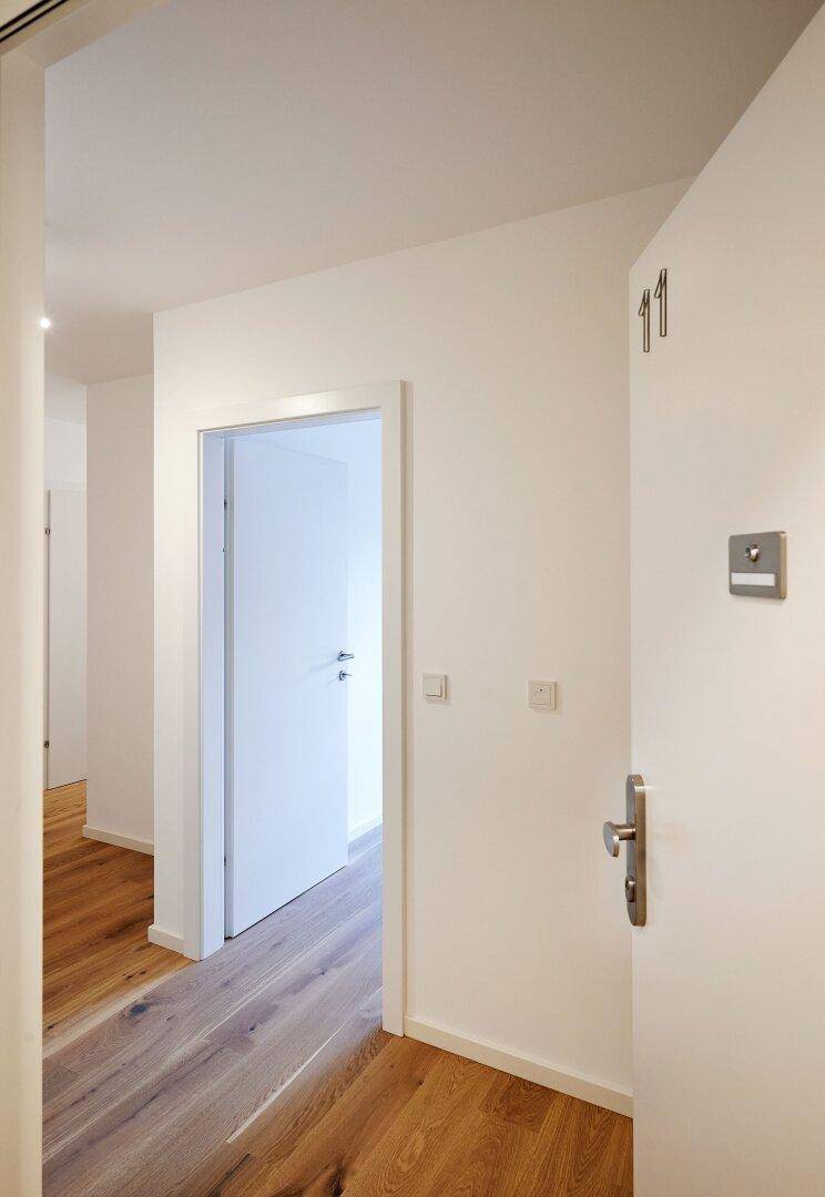 Eingangsbereich mit Holzboden und weißer Tür, die zu den Wohnräumen führt.
