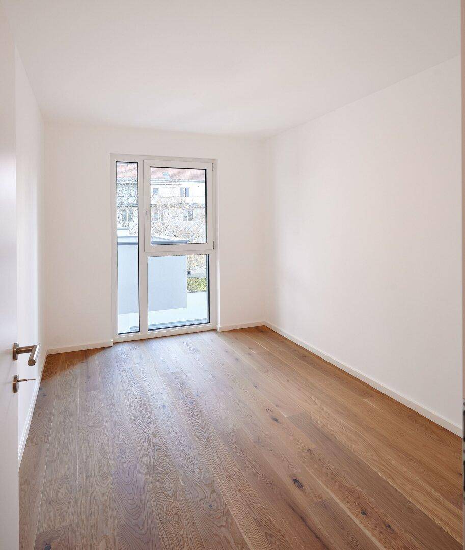 Ruhiges Schlafzimmer mit Holzboden und großem Fenster, das einen Blick ins Grüne ermöglicht.