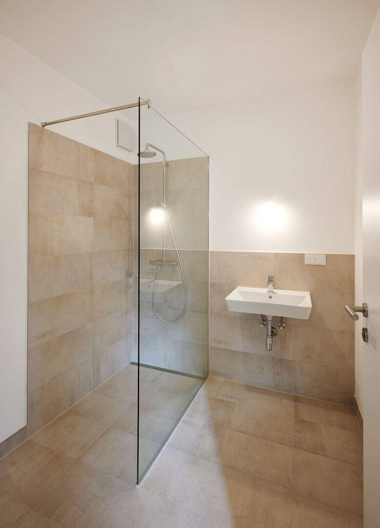 Modernes Badezimmer mit begehbarer Dusche, beigefarbenen Fliesen und einem einzelnen Waschbecken.