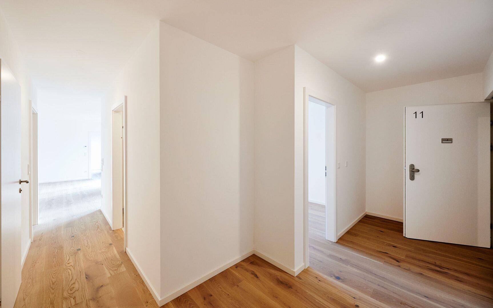 Heller Flur mit Holzboden und mehreren Türen, der verschiedene Räume miteinander verbindet.
