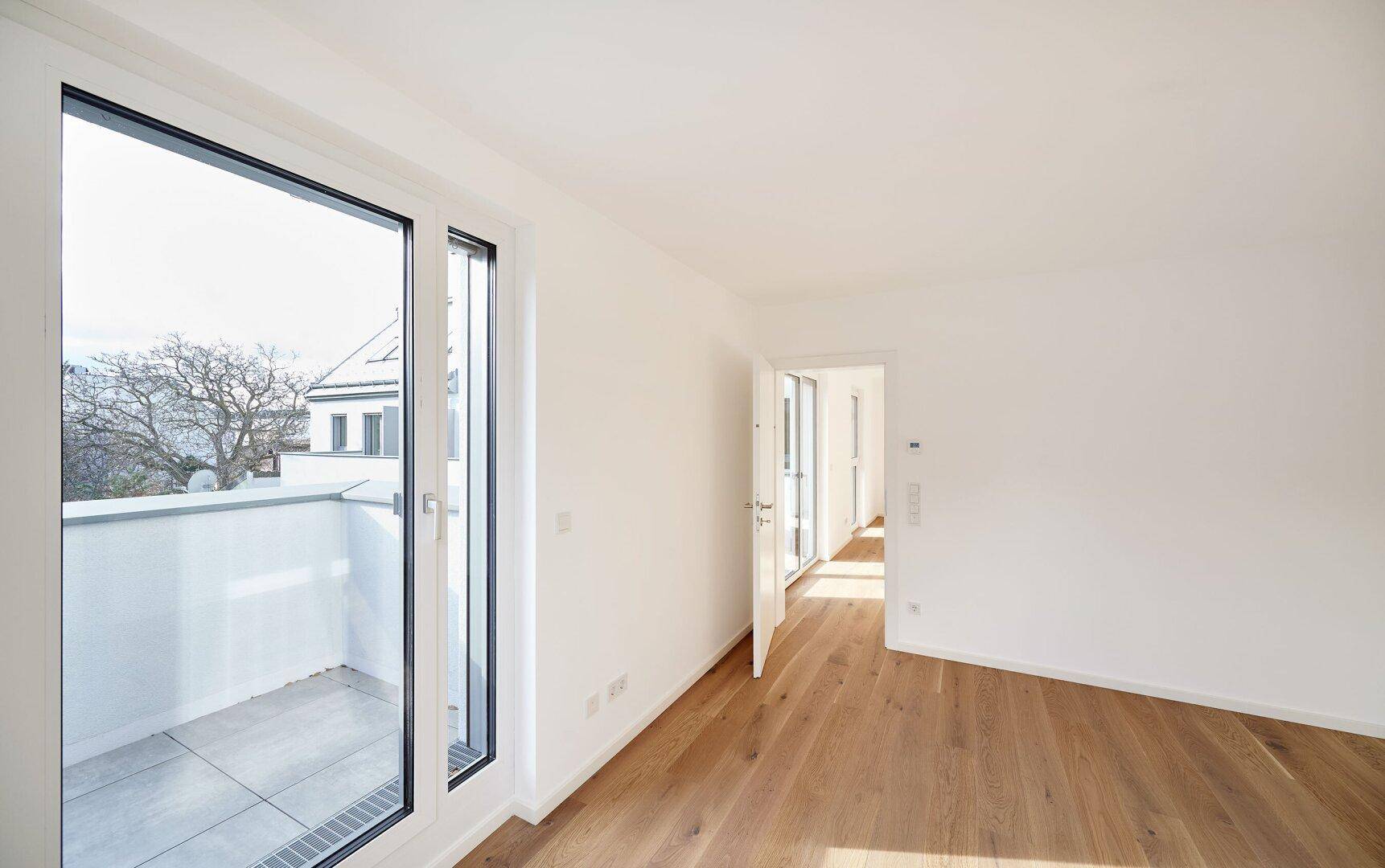 Geräumiges Wohnzimmer mit Holzboden und Balkonzugang, das viel natürliches Licht empfängt.
