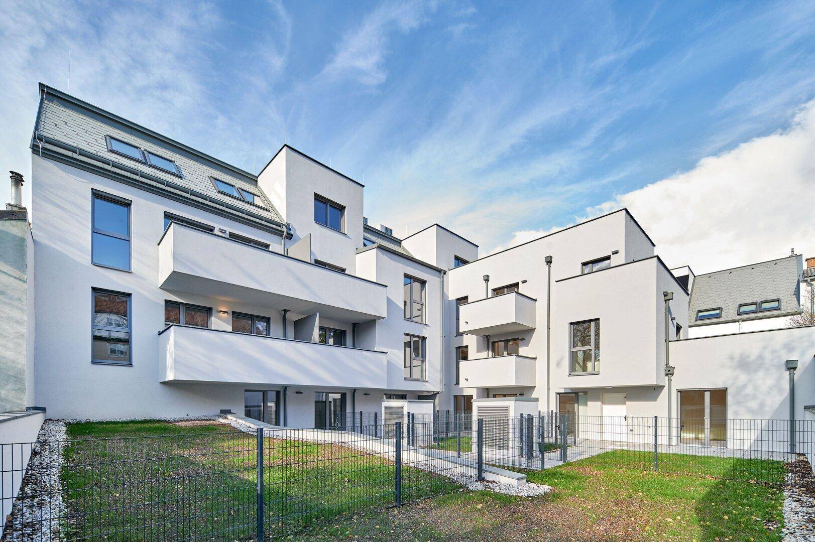 Rückansicht der modernen Wohnanlage mit gepflegtem Rasen und Balkonen unter blauem Himmel.