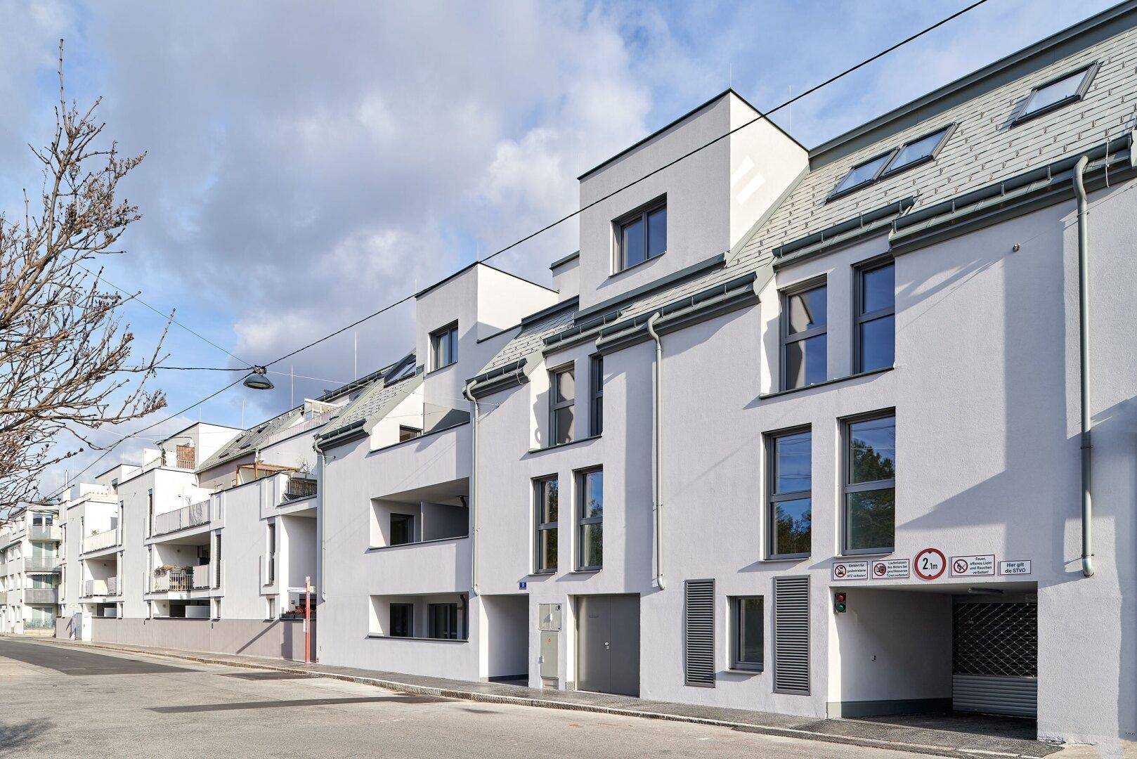 Moderne Wohngebäude mit weißer Fassade, großen Fenstern und Balkonen entlang der Straße.