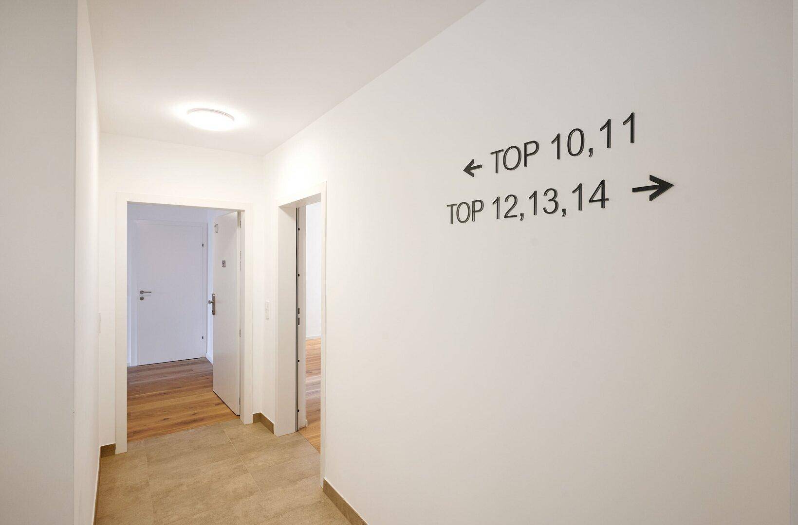 Heller Flur im Gebäude mit Wegweisern zu den verschiedenen Wohneinheiten.