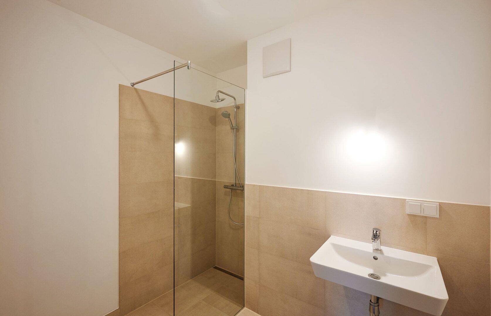 Modernes Badezimmer mit ebenerdiger Dusche, Glaswand und hellem Fliesenboden.