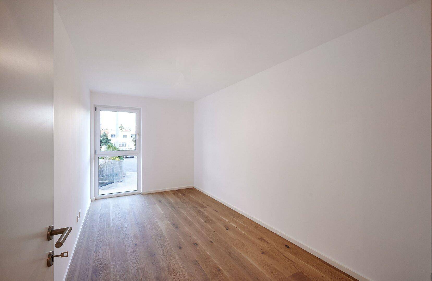 Helles Zimmer mit Holzboden und großem Fenster, geeignet als Schlafzimmer oder Arbeitszimmer.
