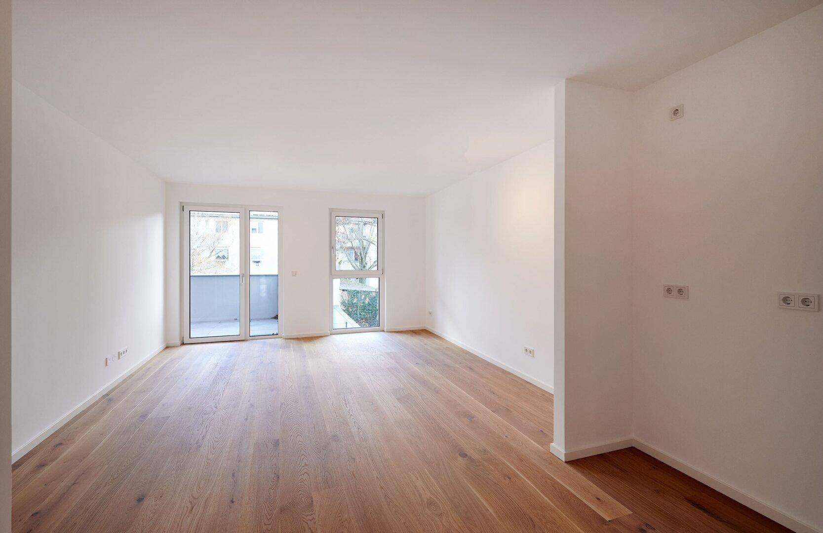 Geräumiges, helles Wohnzimmer mit Holzboden und großen Fenstern, bereit zum Einrichten.