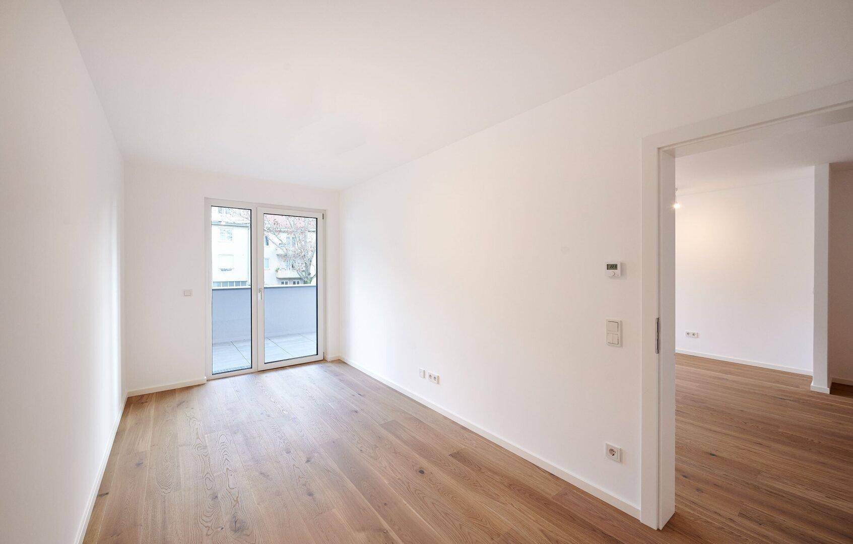 Lichtdurchfluteter Wohnbereich mit Parkettboden und Zugang zum Balkon, ideal für modernes Wohnen.