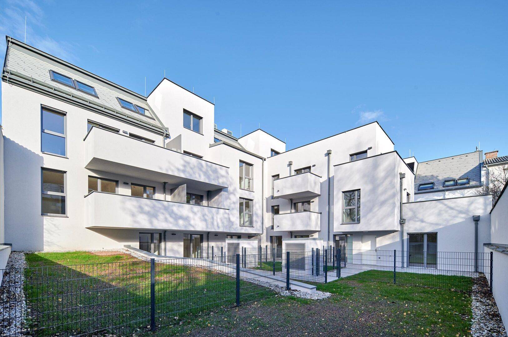 Gesamtansicht der modernen Wohnanlage mit weißer Fassade, Balkonen und begrünten Außenbereichen.
