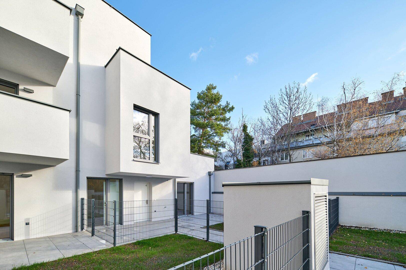 Außenansicht eines modernen Neubaus mit weißer Fassade, Gartenbereich und klarem blauen Himmel.