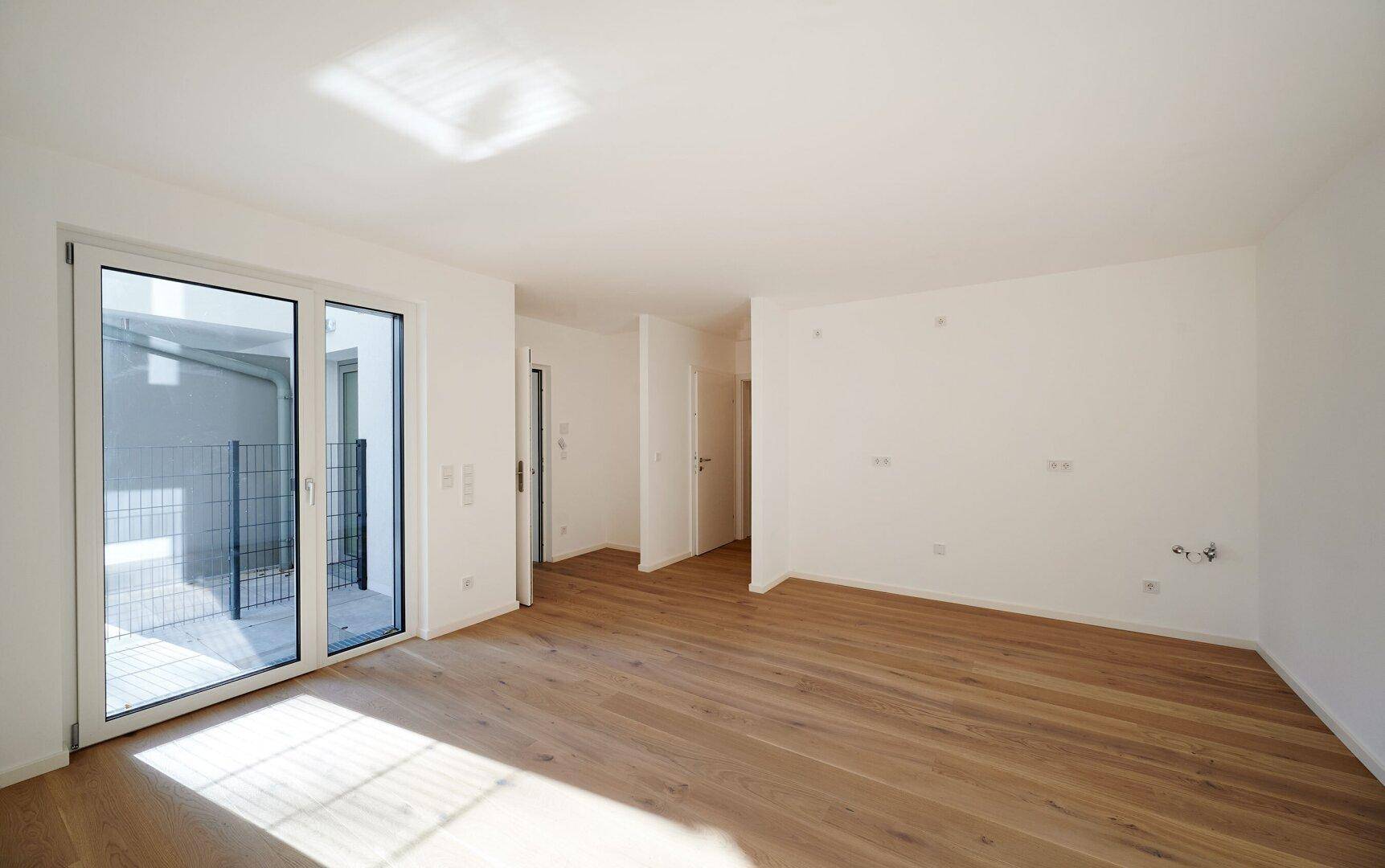 Geräumiges, helles Zimmer mit Holzboden und großen Schiebetüren, die zu einem Außenbereich führen.