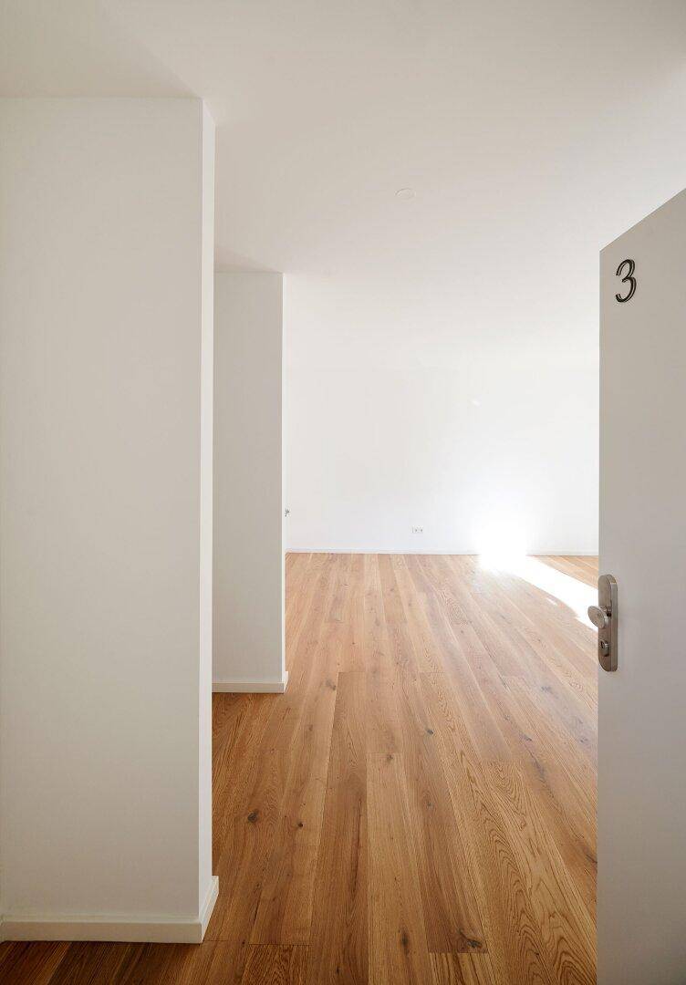 Heller Eingangsbereich mit Holzboden und offener Tür, die zu einem weiteren Zimmer führt.