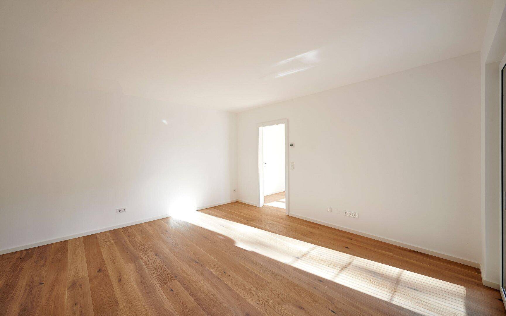 Lichtdurchfluteter Raum mit Holzboden und viel Sonnenlicht, das durch die großen Fenster fällt.