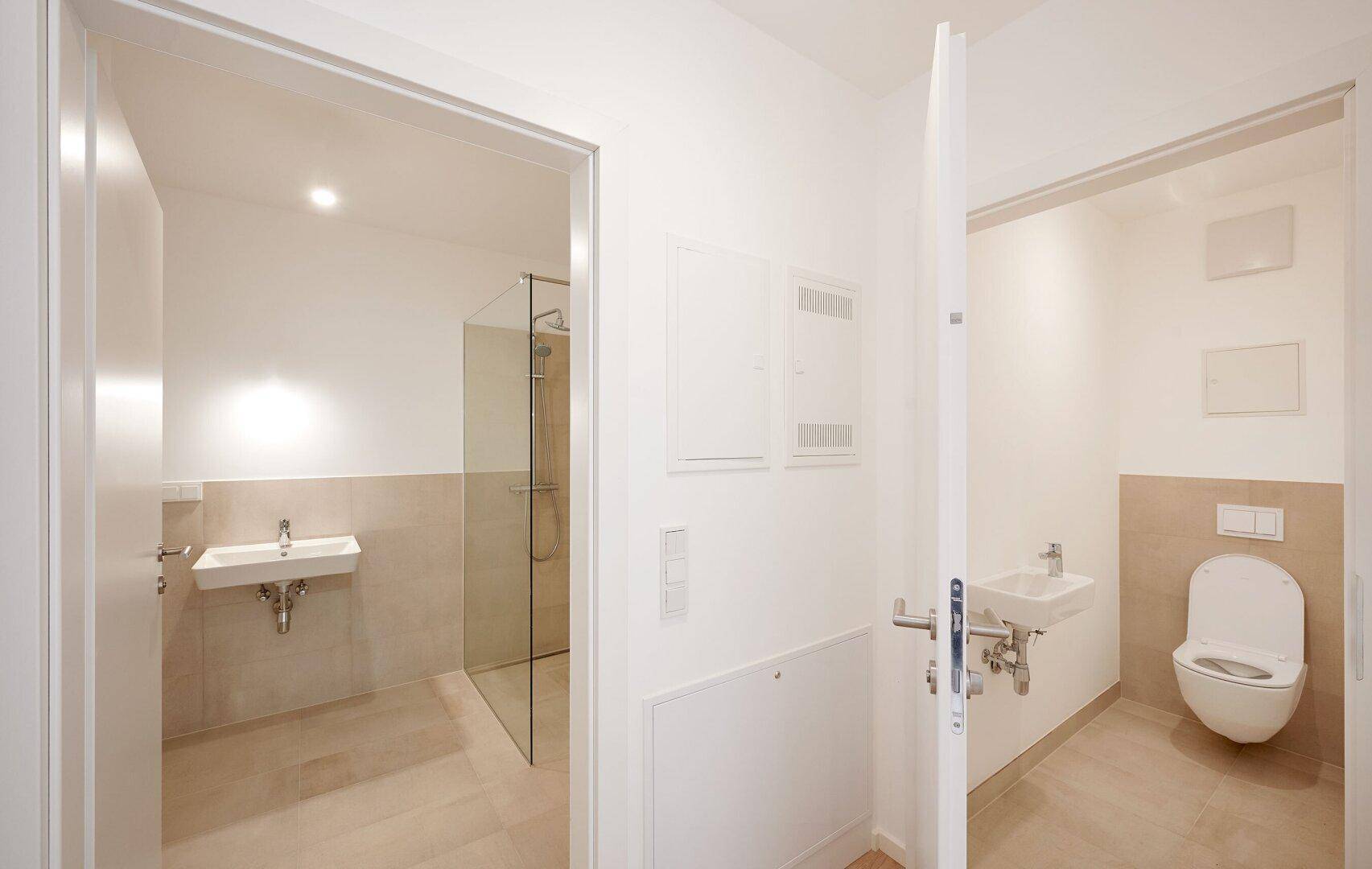 Modernes Badezimmer mit Dusche, Waschbecken und separatem WC-Bereich mit Wand-WC.