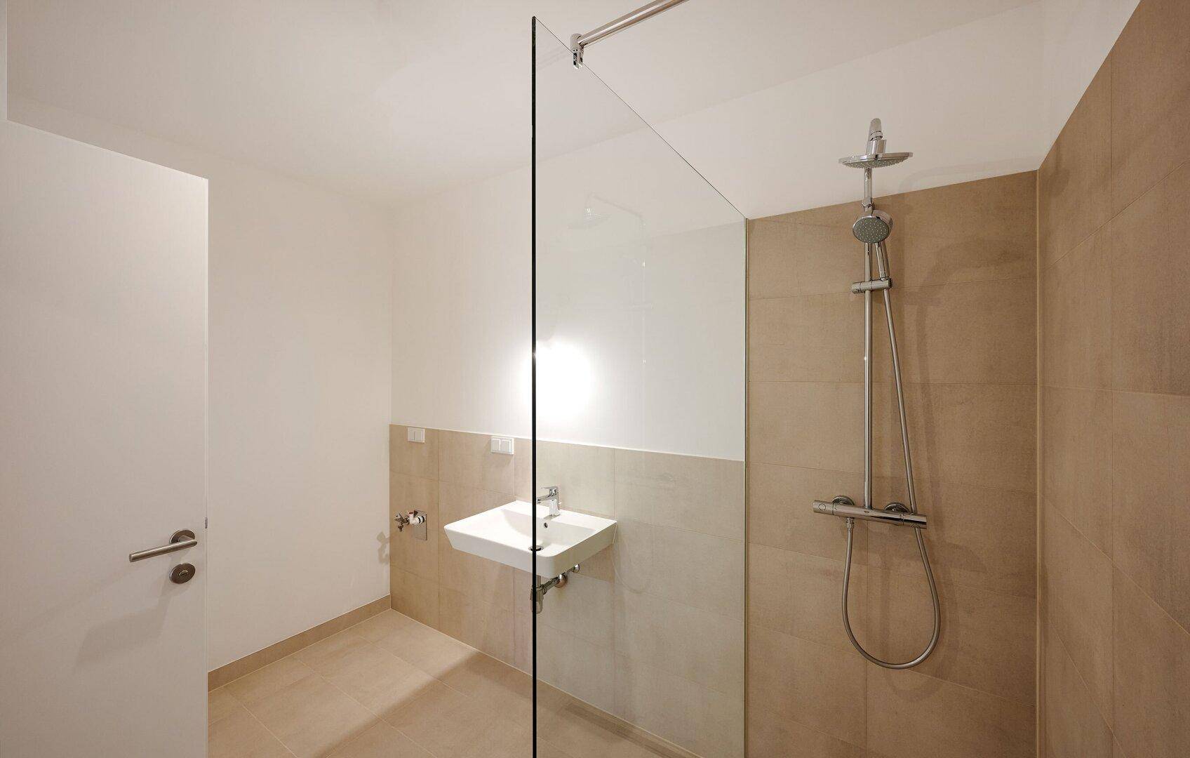 Helle begehbare Dusche mit Glaswand und modernem Waschbecken in einem neuen Badezimmer.