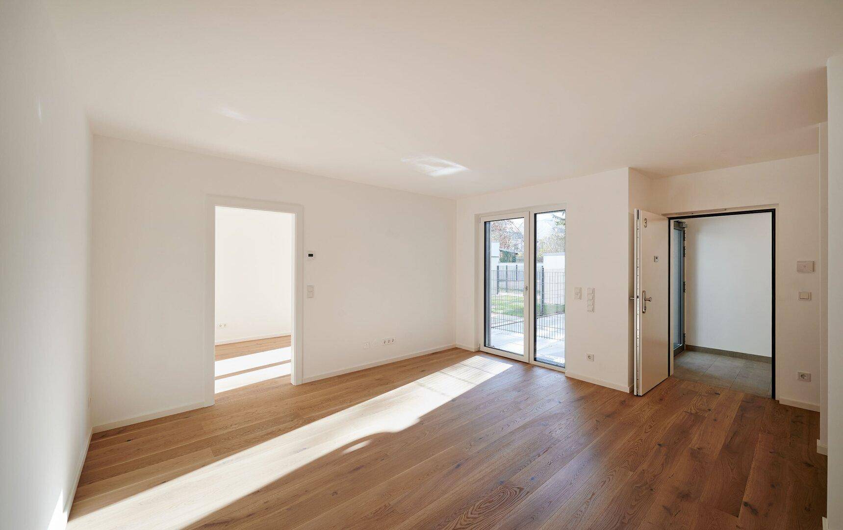 Großes, helles Zimmer mit Holzboden und Schiebetüren, die zu einem Gartenbereich führen.