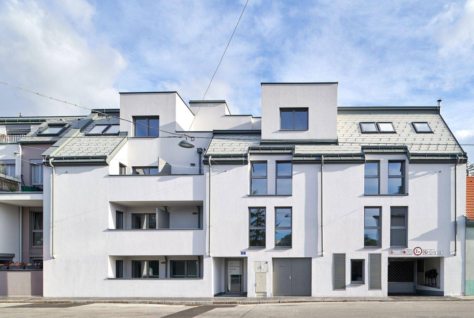 Ansicht der modernen Wohnhausfassade mit klaren Linien und verschiedenen Fensterformen.