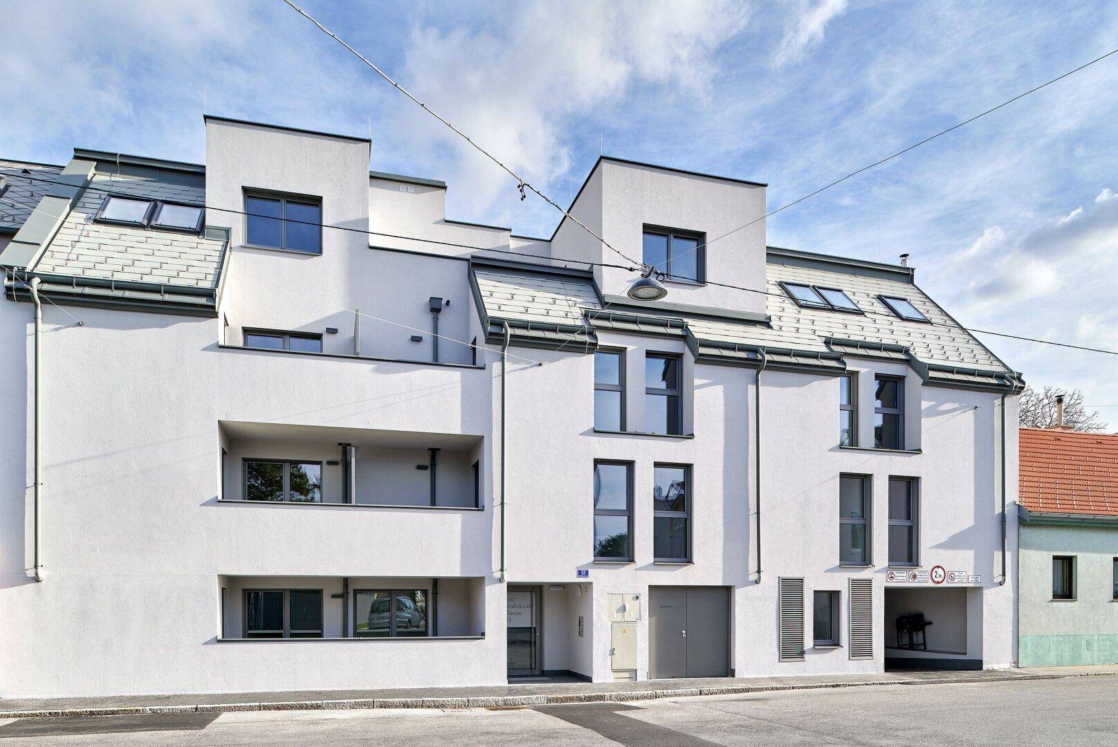 Straßenansicht eines zeitgenössischen Wohngebäudes mit weißer Putzfassade und Dachfenstern.
