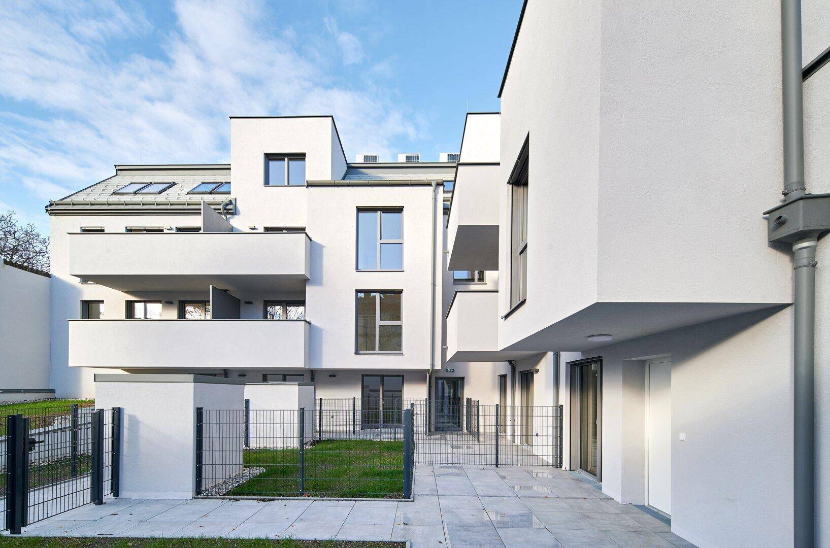 Moderne Wohnanlage mit weißer Fassade, Balkonen, Terrasse und einem kleinen Gartenbereich.
