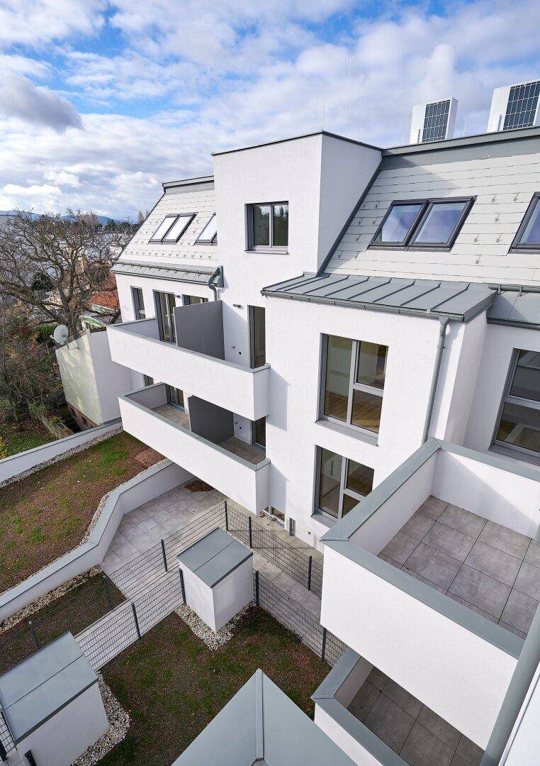 Luftaufnahme der modernen Wohnanlage mit mehreren Terrassen und Balkonen unter blauem Himmel.