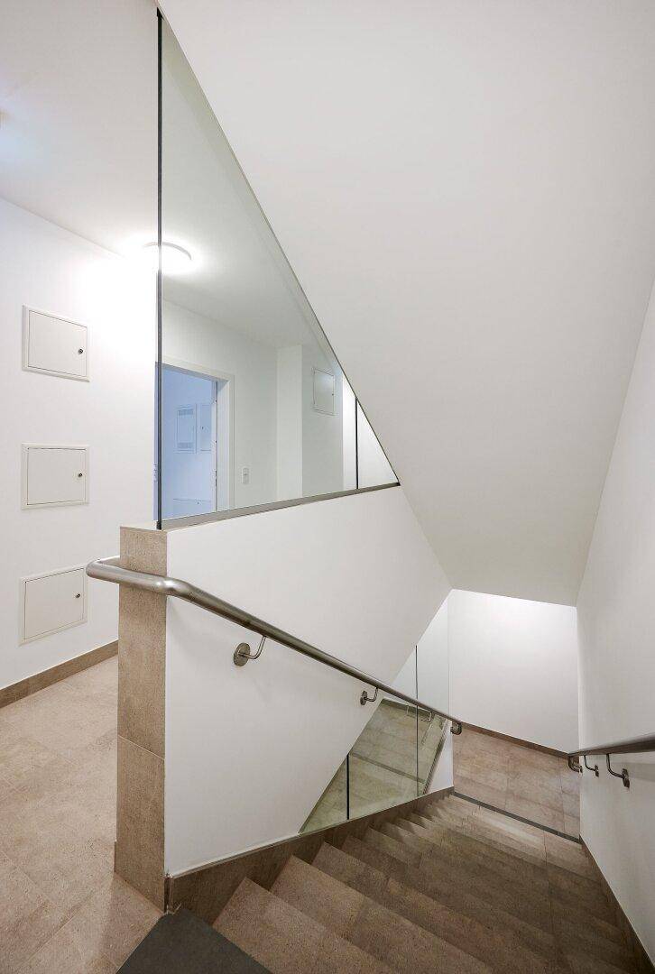 Treppenhaus mit modernem Design, Glasgeländer und Fliesenboden.