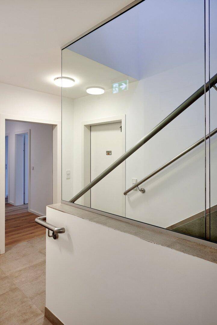 Moderner Treppenaufgang mit Glasgeländer und Zugang zu den Wohneinheiten.
