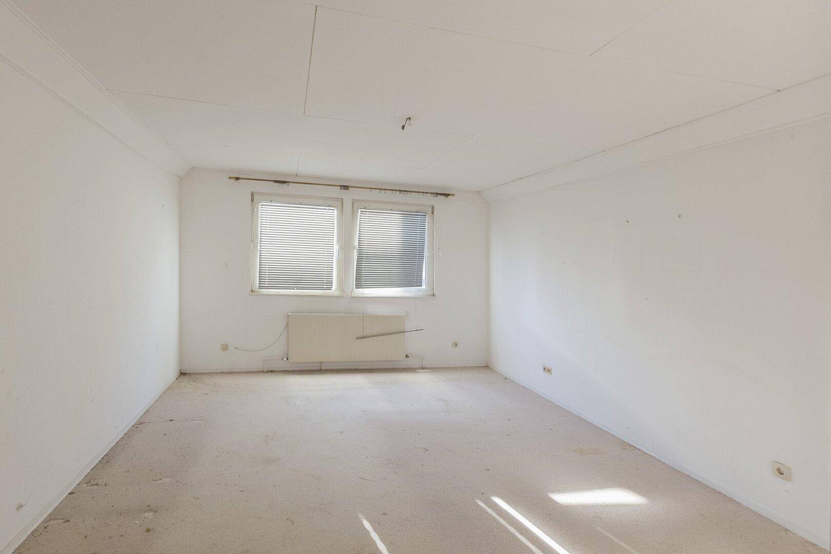 Leeres Schlafzimmer mit Teppichboden und einem Fenster mit Jalousien, bereit zur individuellen Gestaltung.