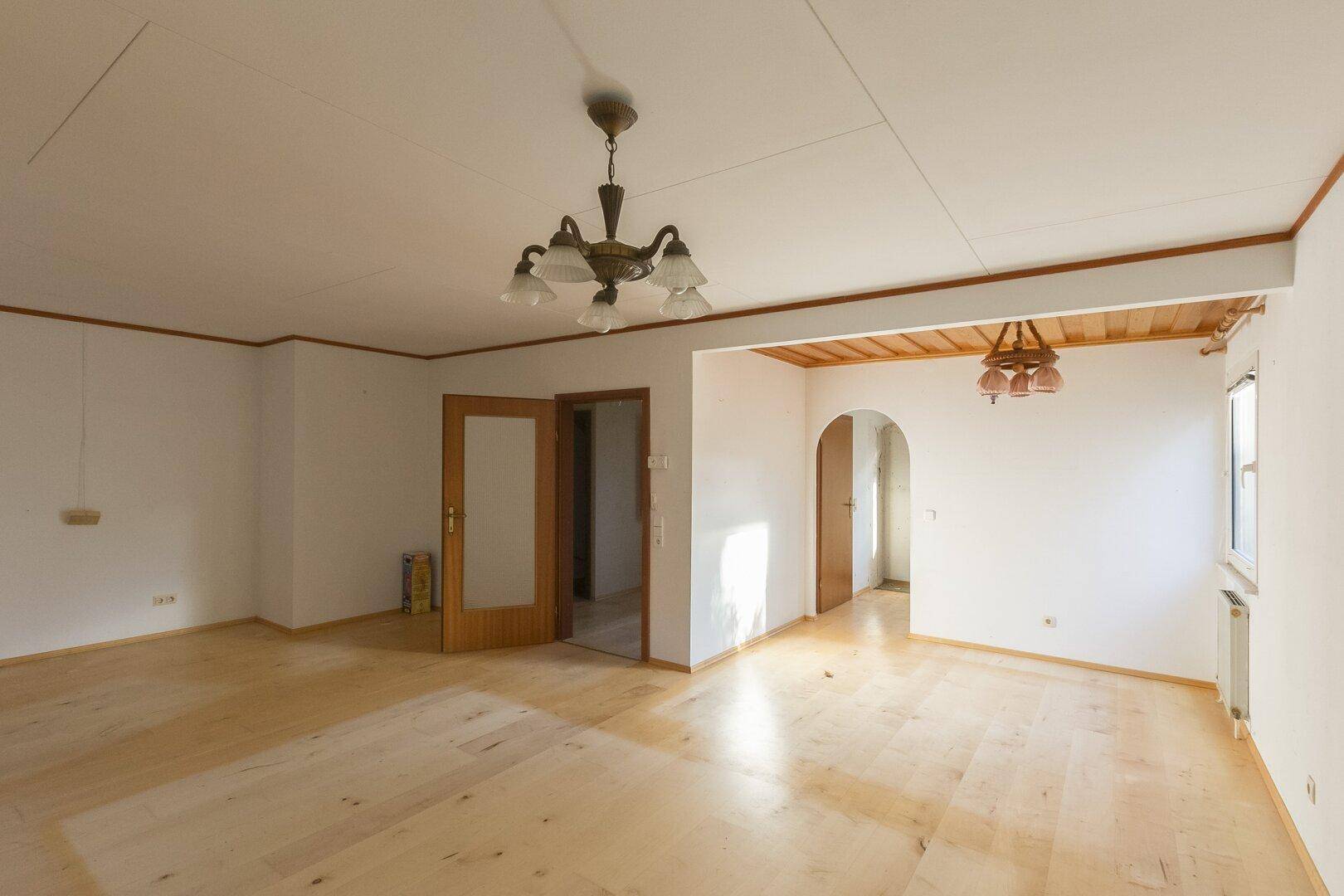 Geräumiger Wohnbereich mit Holzboden, Holztüren und Deckenpaneelen, der zu weiteren Räumen führt.