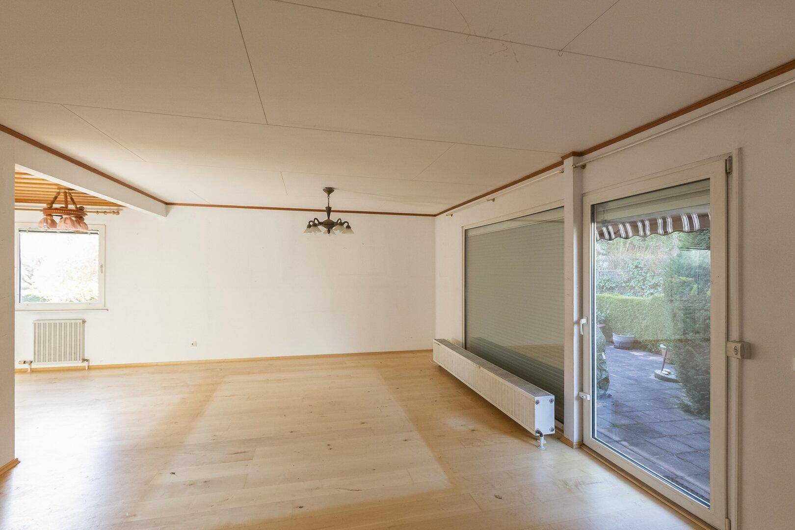 Helles, leeres Wohnzimmer mit Holzboden, großen Fenstern und Zugang zur Terrasse.