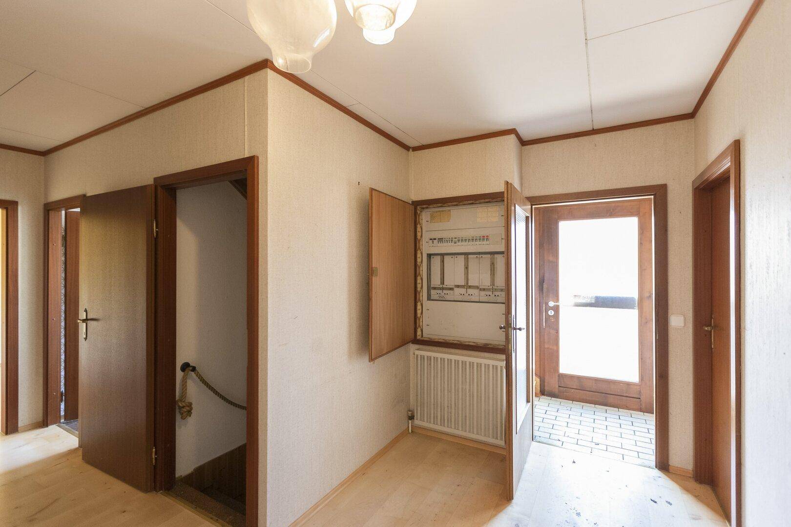 Eingangsbereich oder Flur mit Holzboden, Heizkörper und offenem Sicherungskasten.