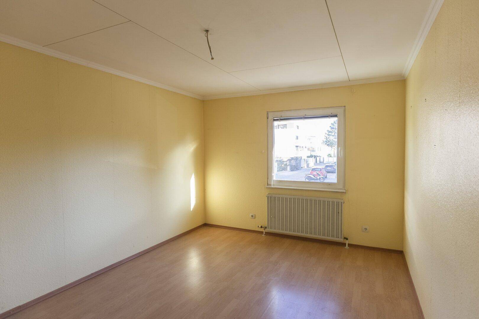 Helles Schlafzimmer mit gelben Wänden, Holzboden und einem Fenster mit Blick nach draußen.