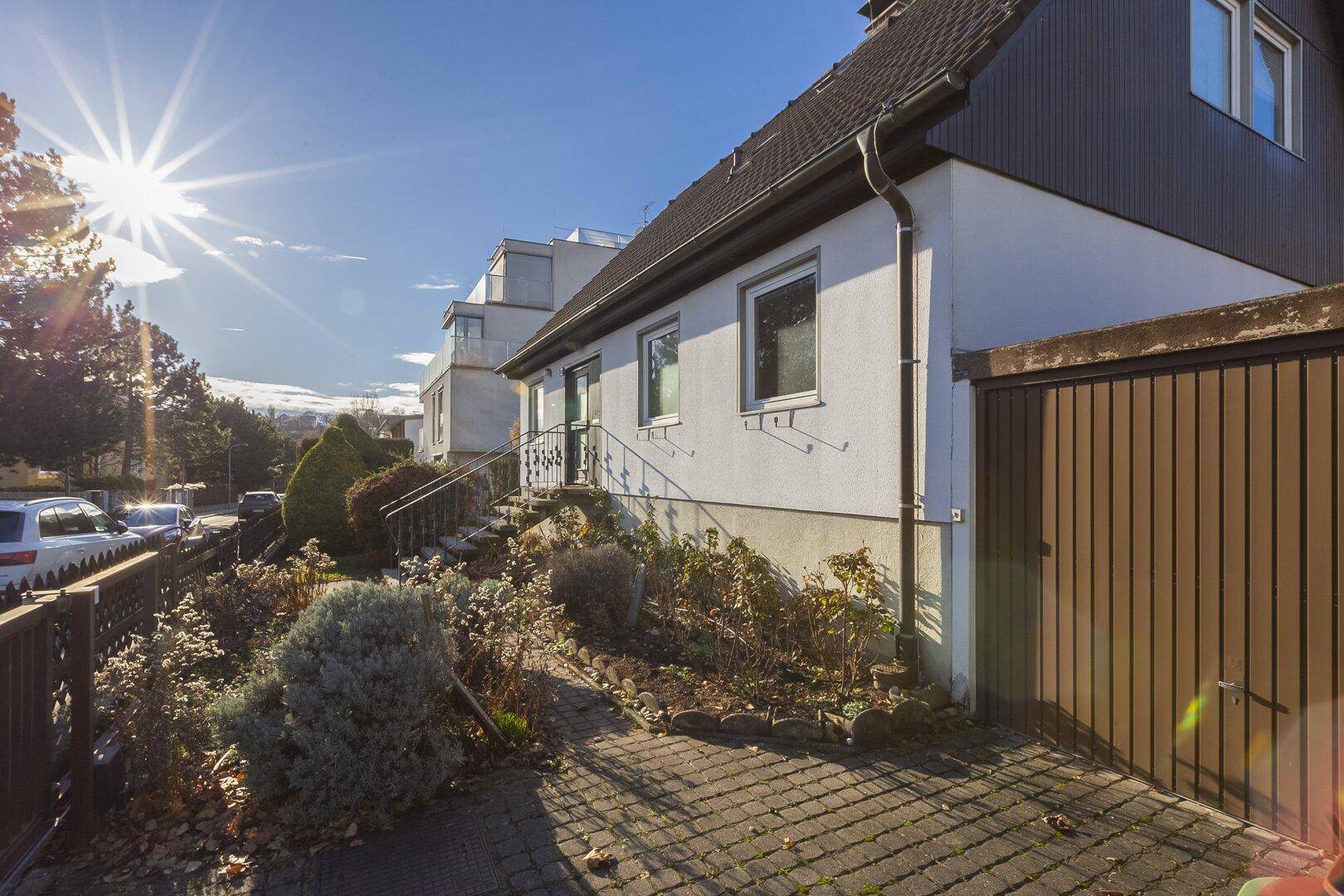 Seitenansicht des Hauses mit gepflasterter Auffahrt, Gartenbereich und Sonneneinstrahlung.