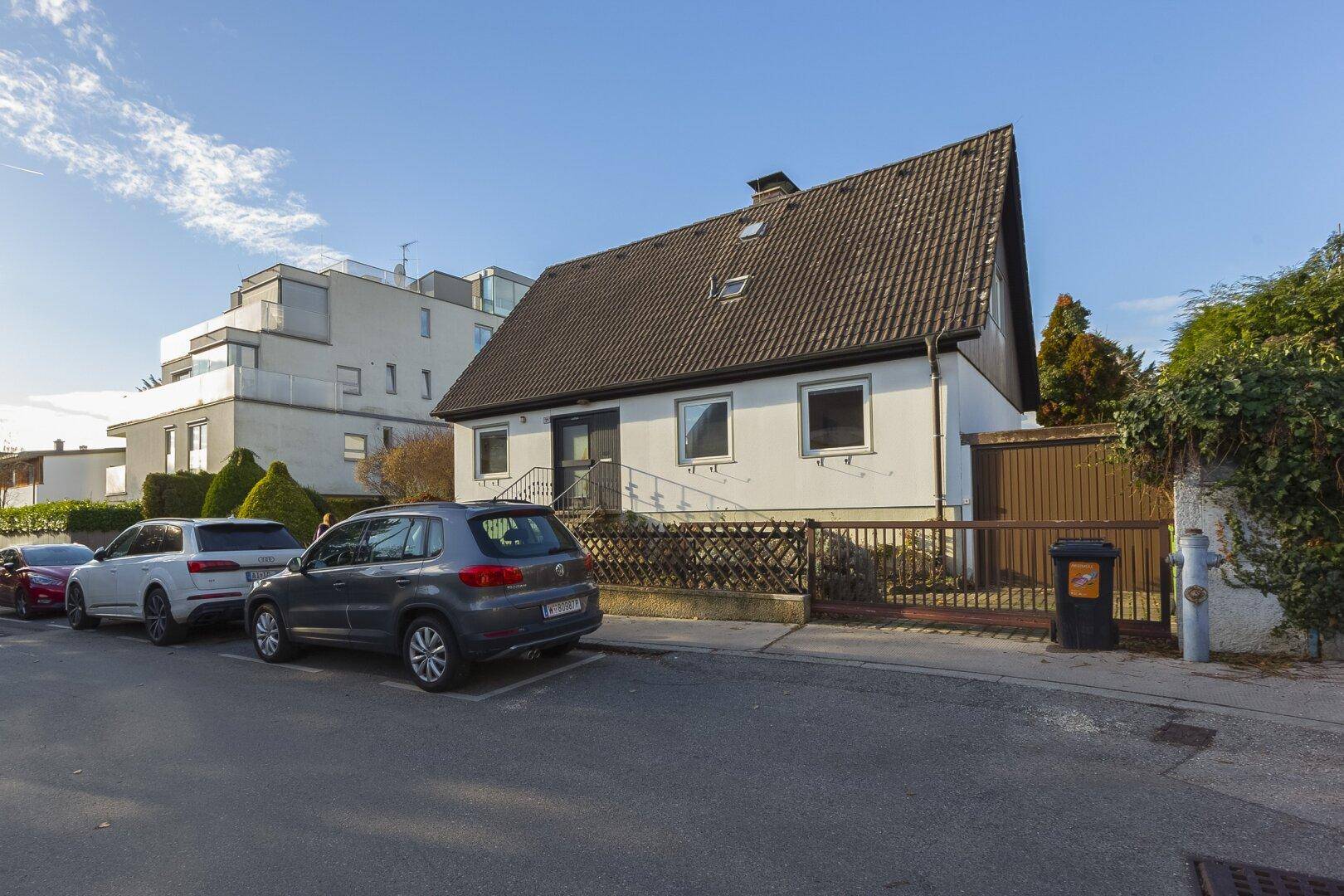 Seitenansicht des Einfamilienhauses von der Straße, mit Zaun und angrenzenden Gebäuden.