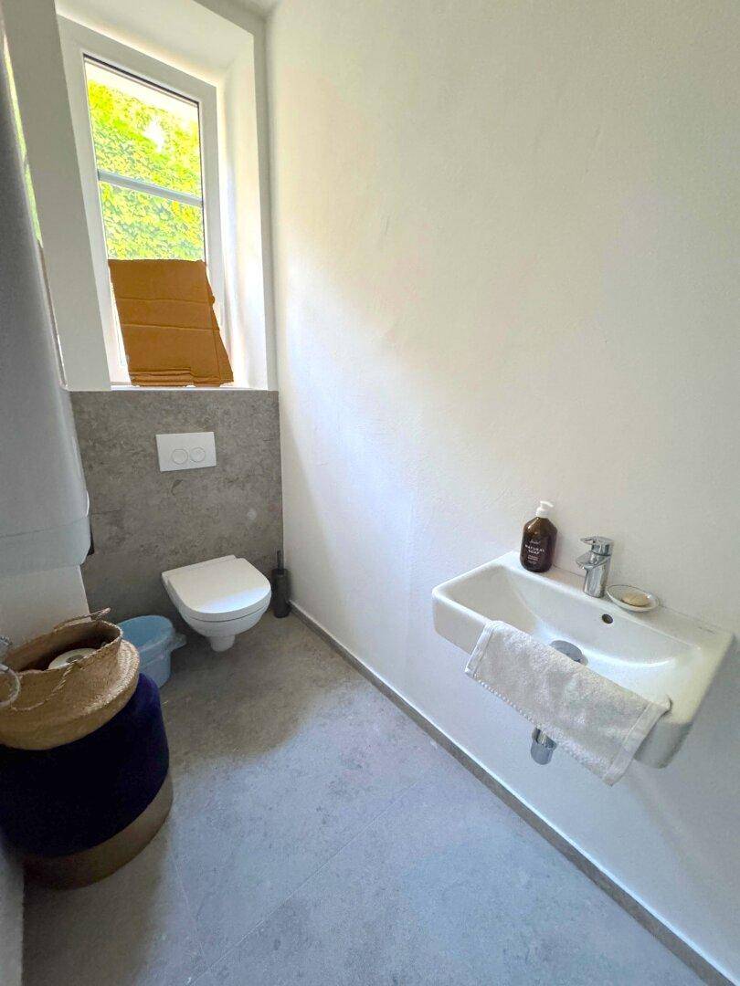 Kleines WC mit wandhängender Toilette, Waschbecken und Fenster für Tageslicht.