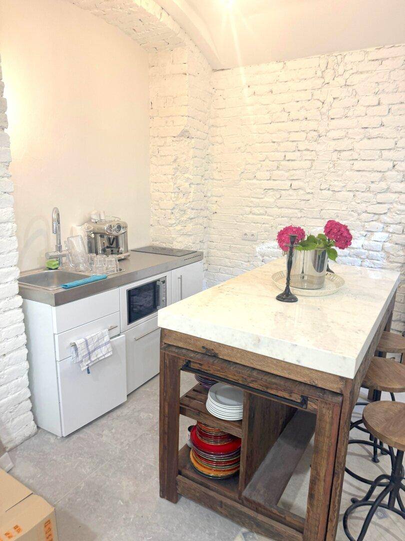 Kleine Küchenzeile mit Spüle und Mikrowelle, ergänzt durch einen Holztisch mit Marmorplatte.