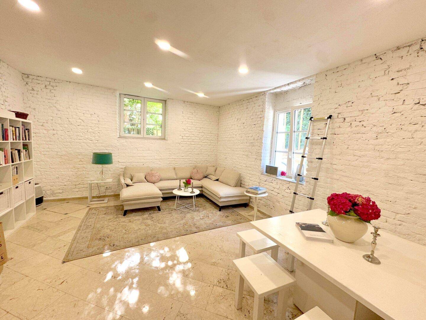 Gemütliches Wohnzimmer mit weiß gestrichenen Ziegelwänden, Ecksofa und Fliesenboden.