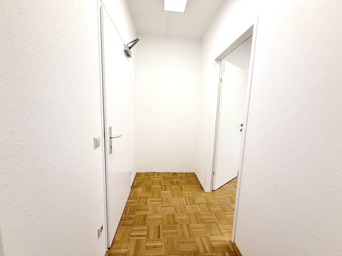 Heller Flur mit Parkettboden und weißen Wänden, der zu weiteren Räumen führt.